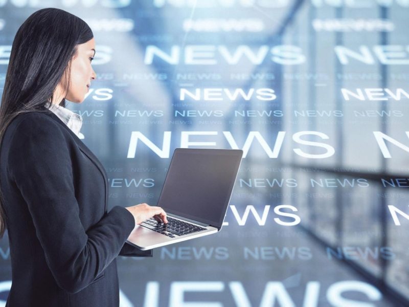Business professional working on a laptop with news headlines behind her