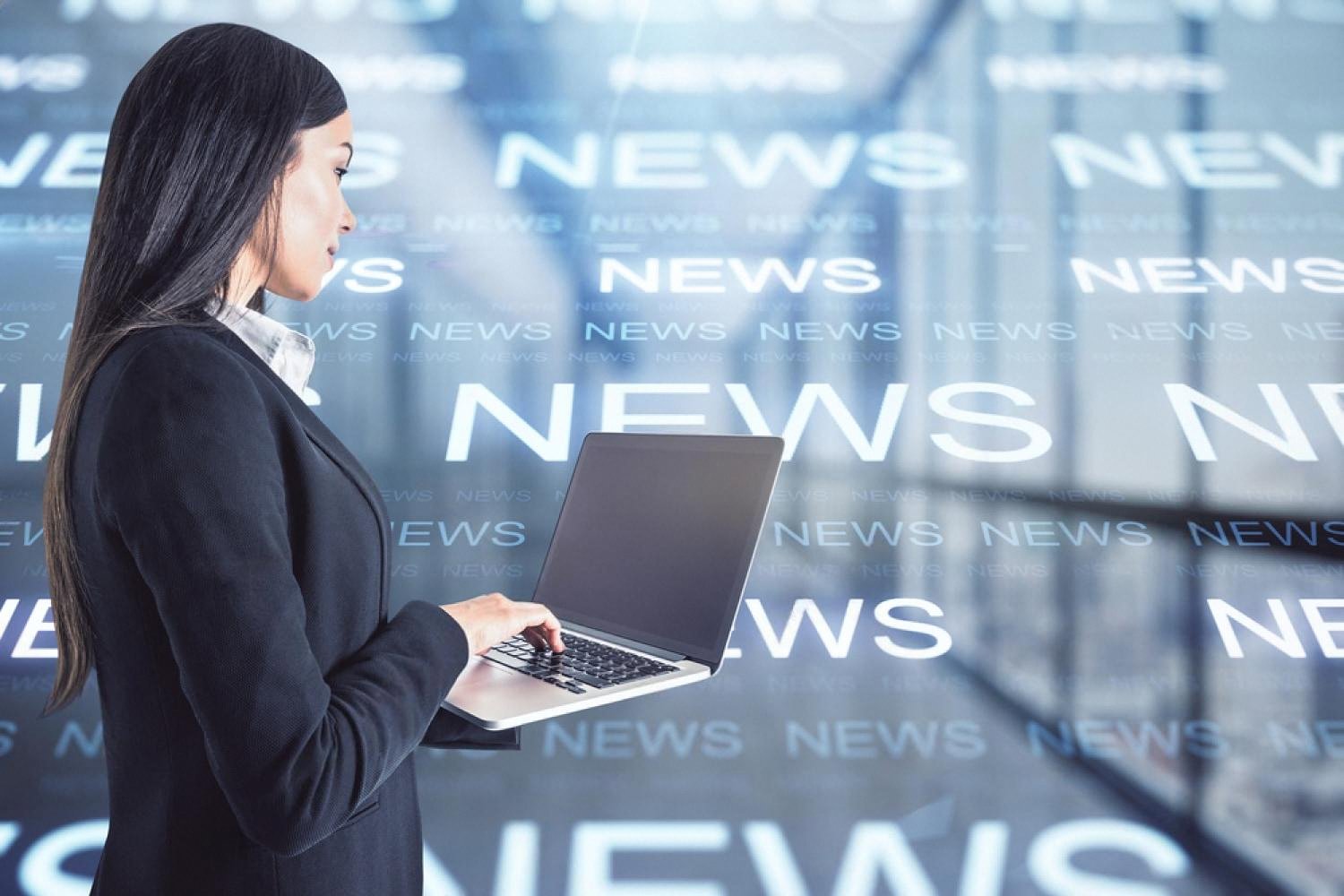 Business professional working on a laptop with news headlines behind her